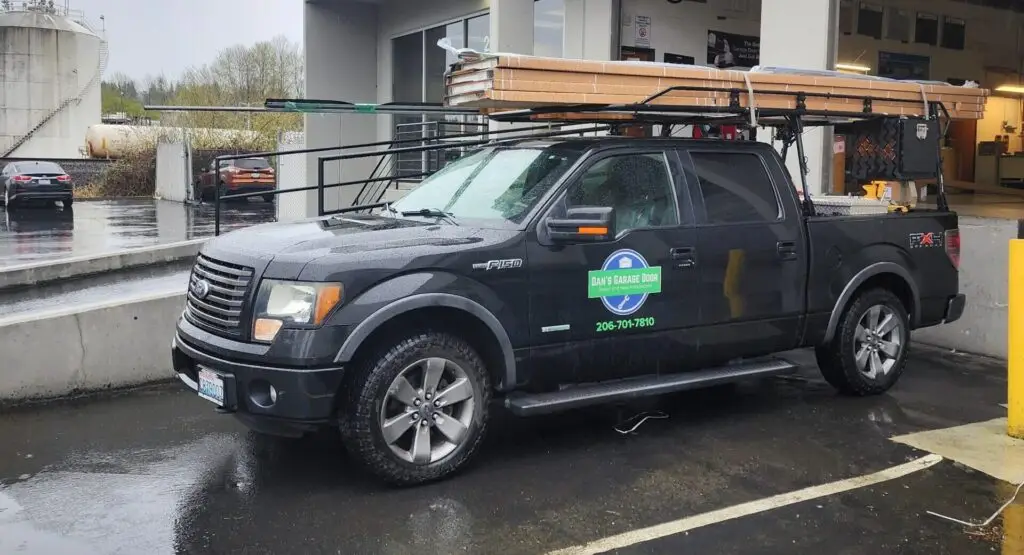 Black pickup truck equipped with tools and ladders, parked outside a facility.