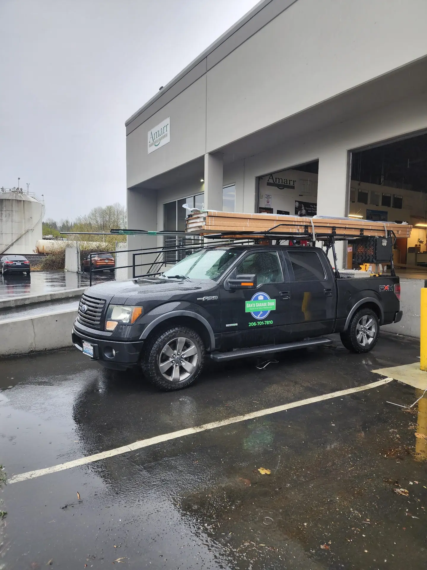 Black truck from Dan's Garage Door parked outside a warehouse on a rainy day, loaded with garage door panels and equipment.