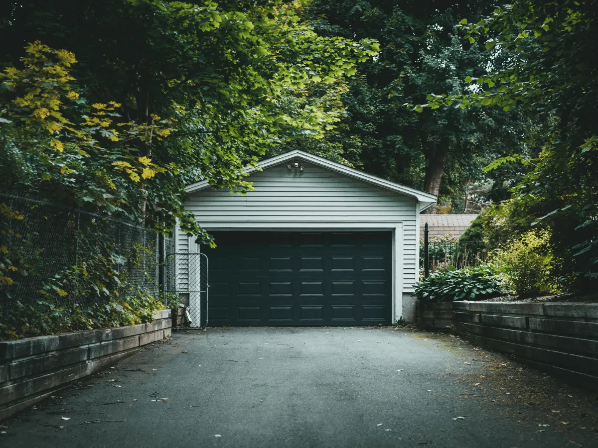 Garage door framed by dense green trees and shrubs