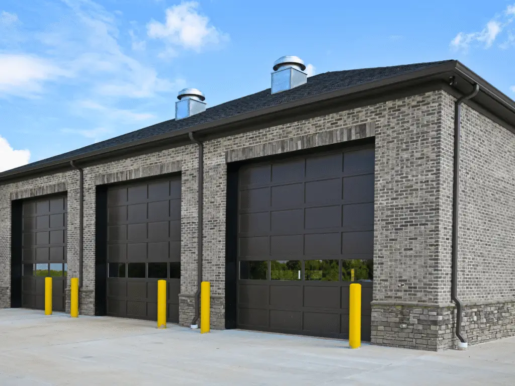 Modern commercial building with three large dark garage doors and brick exterior.