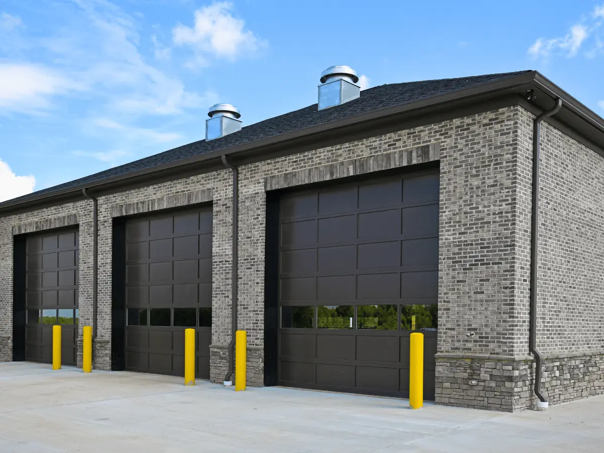 Brick commercial building with three large dark garage doors and yellow bollards