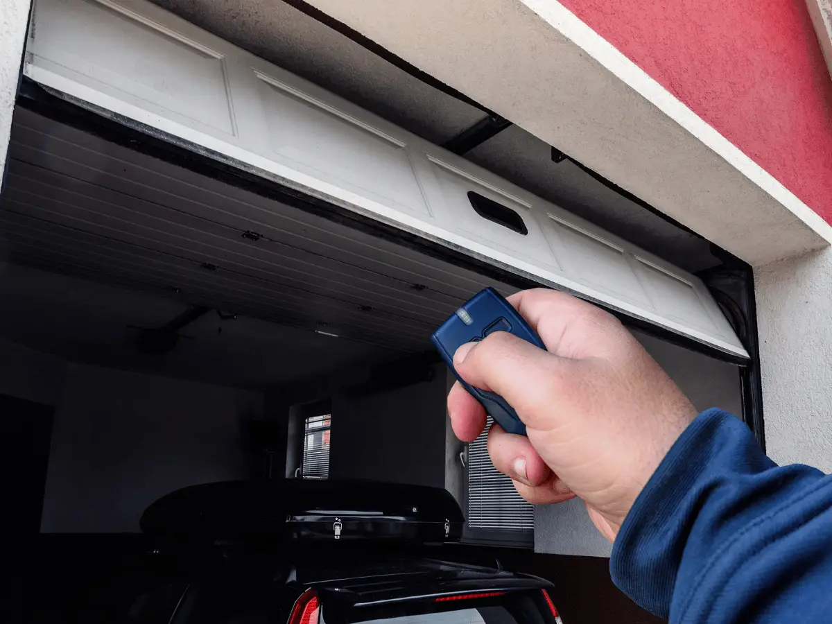 Hand holding blue garage door remote opening a white door