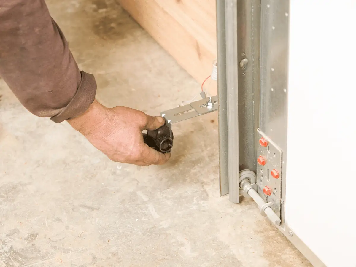 Hand adjusting a black garage door safety sensor near the track