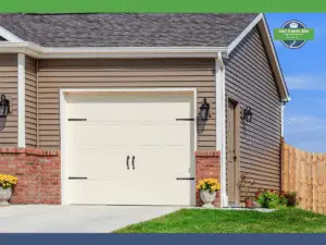 White garage door with black handles beside a man door, surrounded by flowers and a wooden fence.