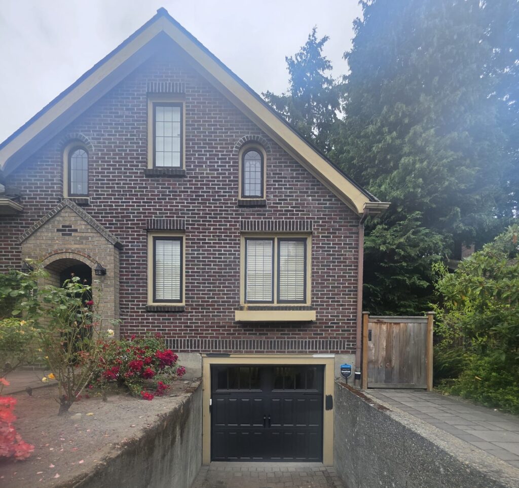 Black garage door beneath brick house at driveway end