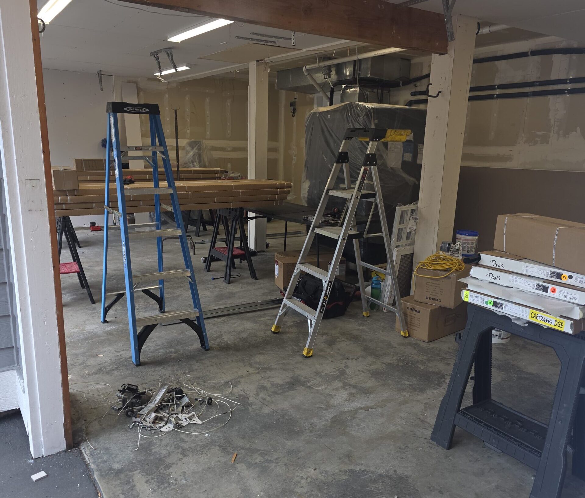 Garage renovation with ladders, boxes, sawhorses, and exposed wiring
