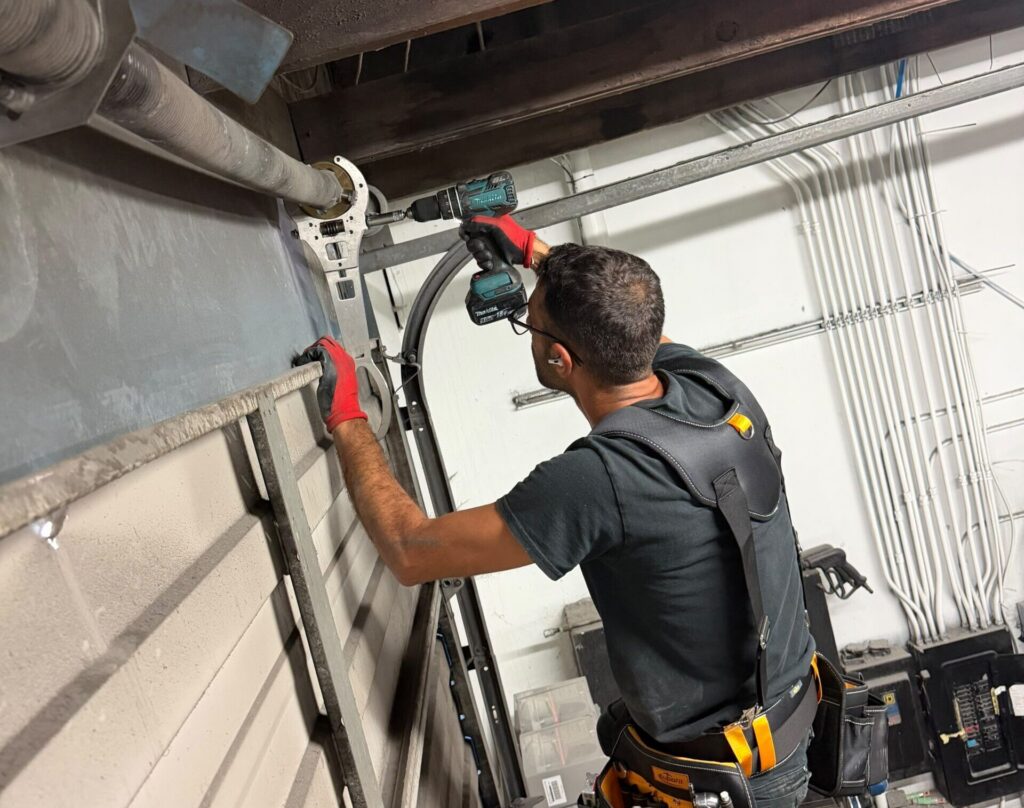 Technician using power drill on industrial overhead door mechanism