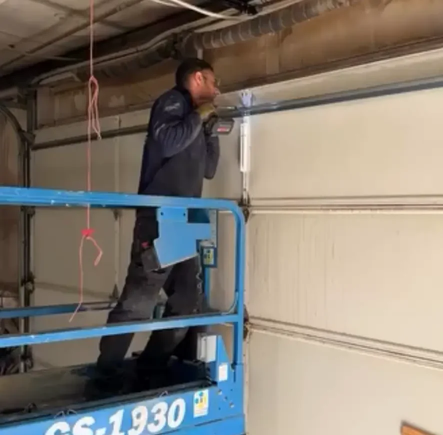 Technician on blue scissor lift working on a garage door opener