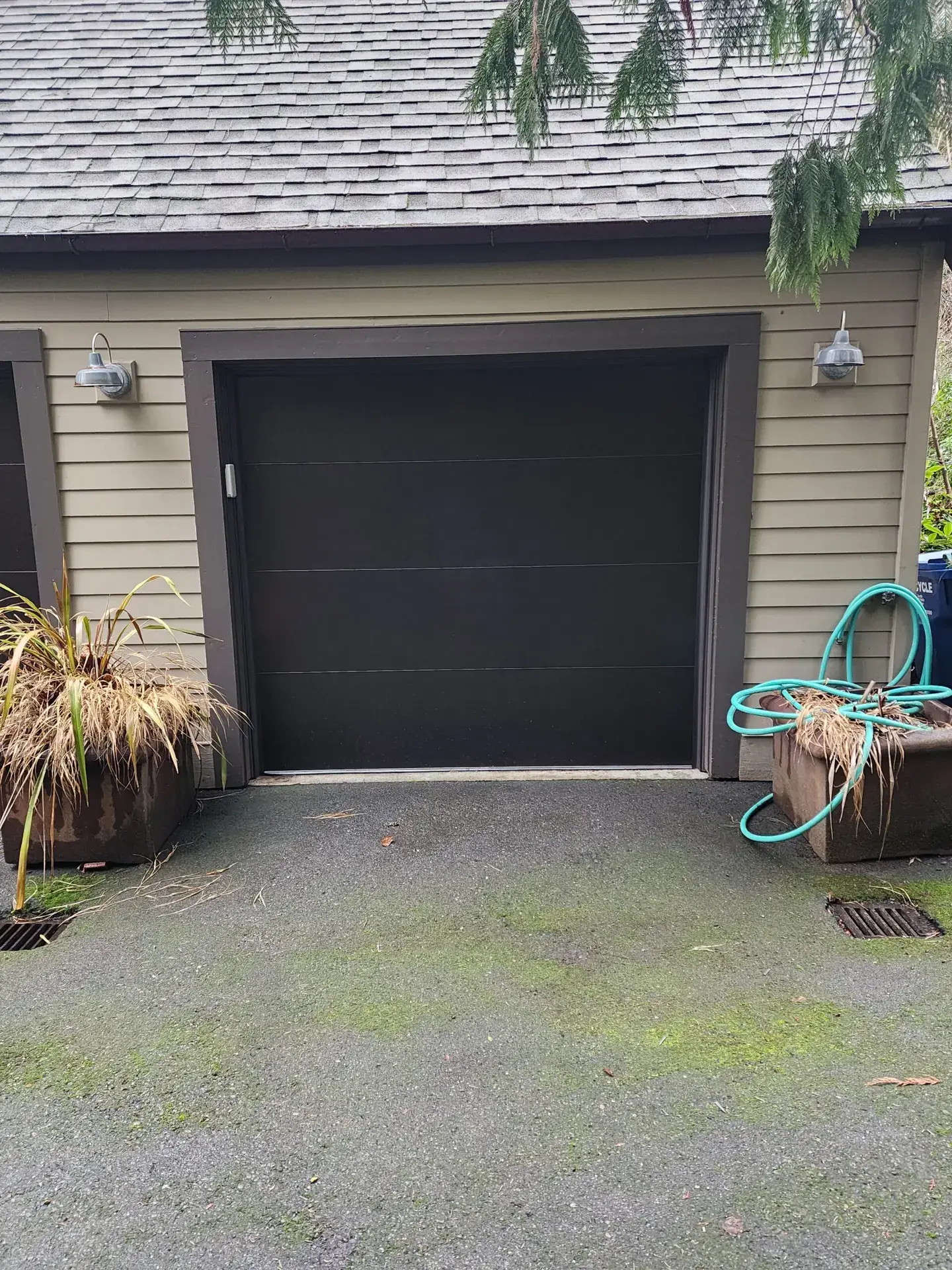 Black garage door beside mossy driveway and potted plants