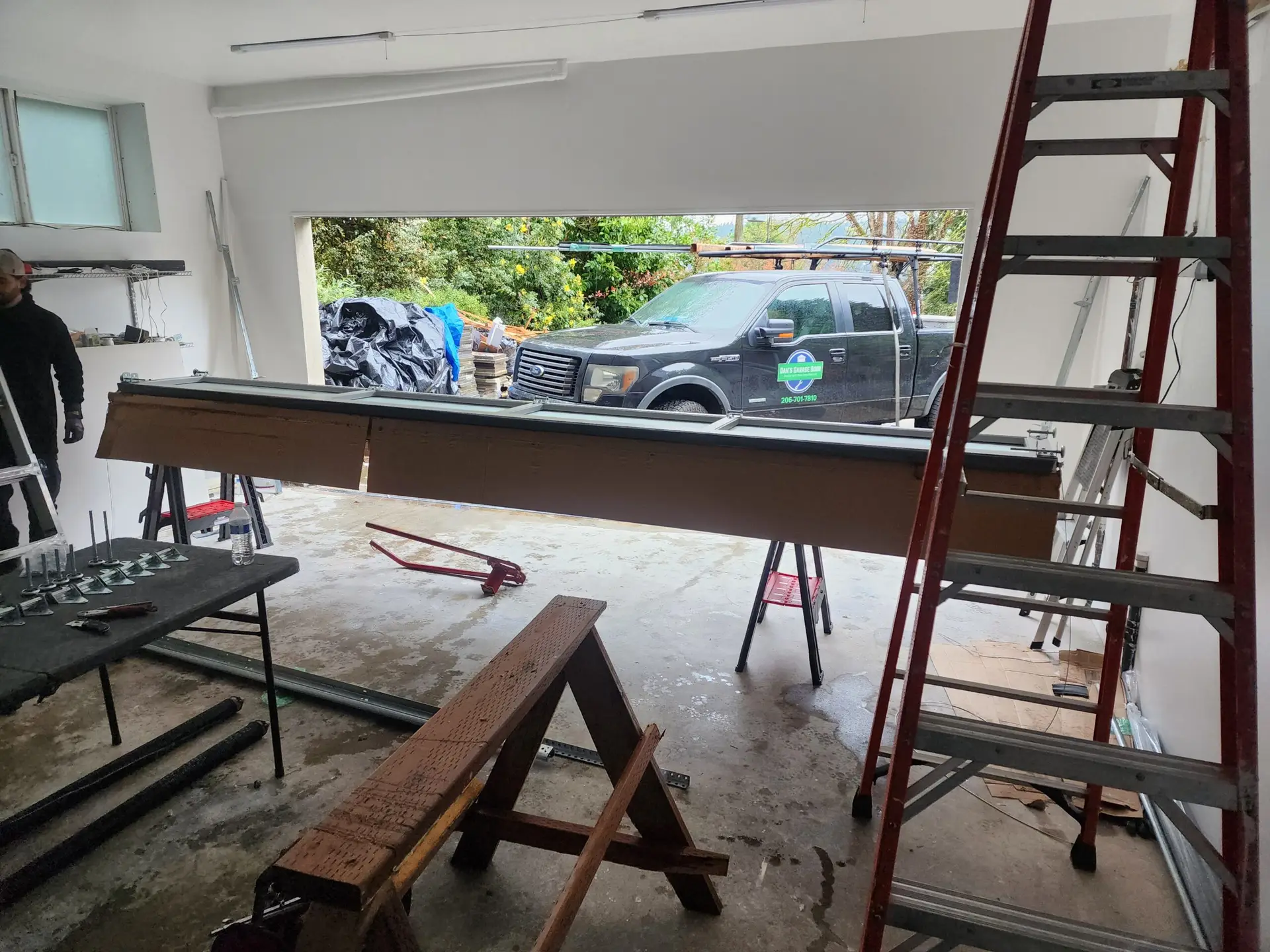 Garage interior with red ladder, sawhorses, and pickup truck outside