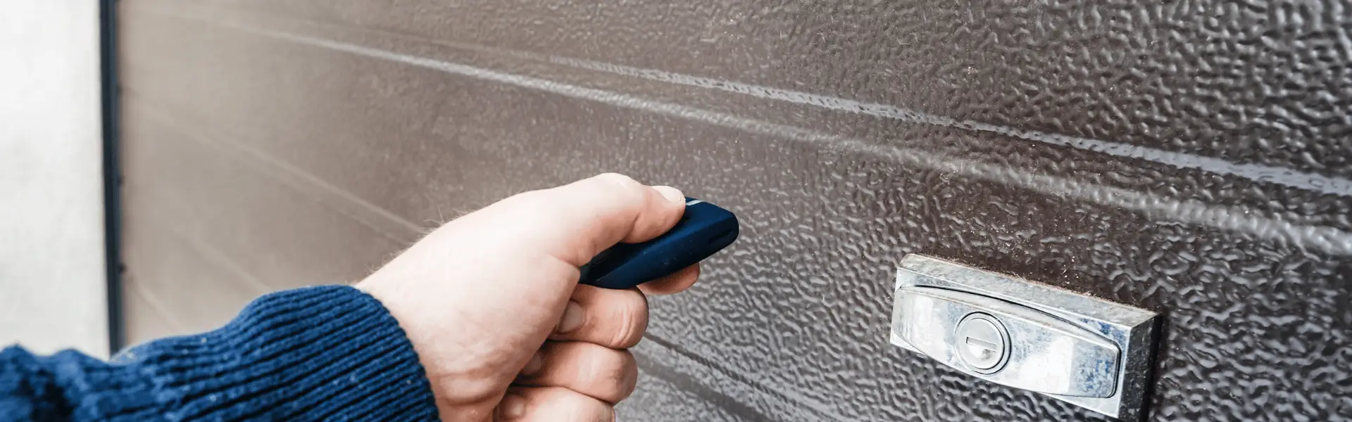 Hand holding a black remote near a metal door lock