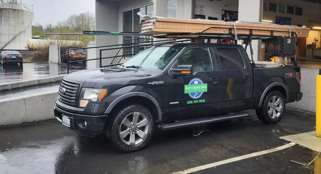 Black Ford F-150 pickup with ladder rack and lumber on top, wet lot