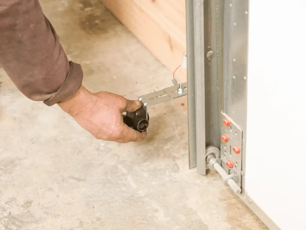 Hand adjusting a black garage door safety sensor near the track