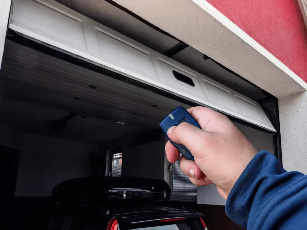 Hand holding blue garage door remote opening a white door