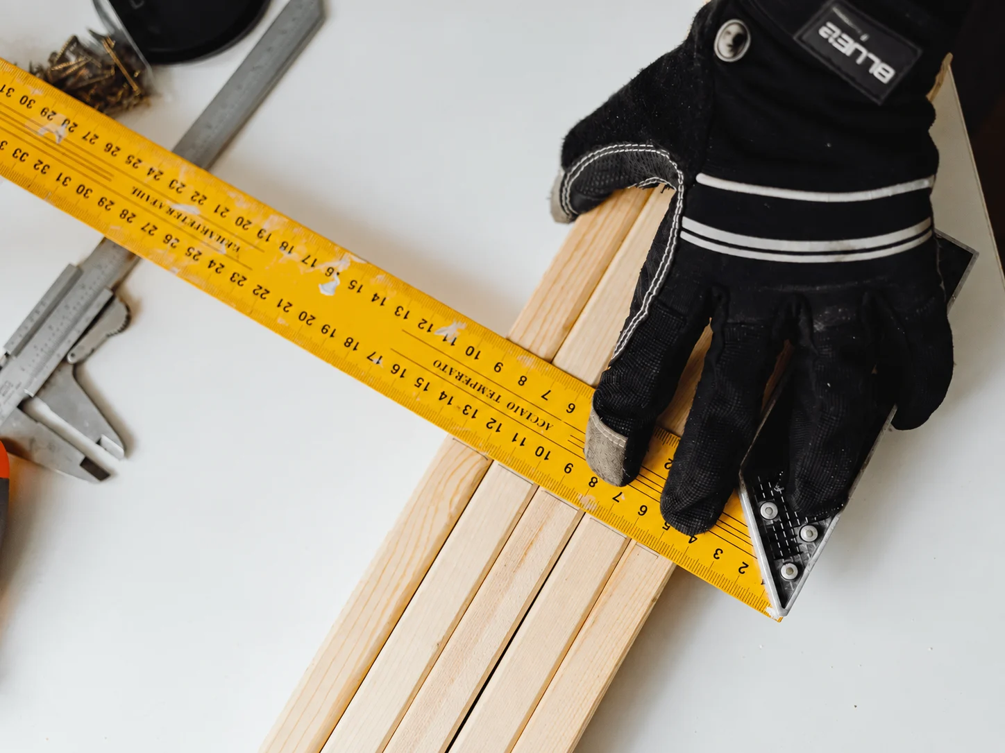 Gloved hand measuring wooden planks with a yellow tape measure