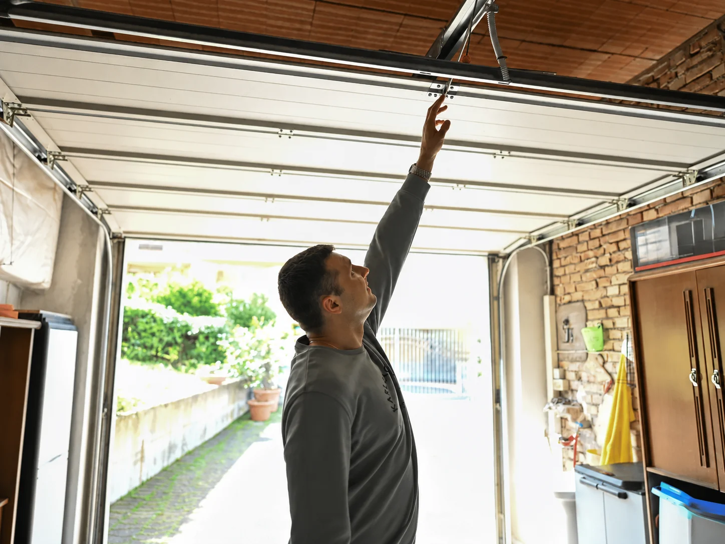 Man inspecting garage door opener mechanism inside open garage