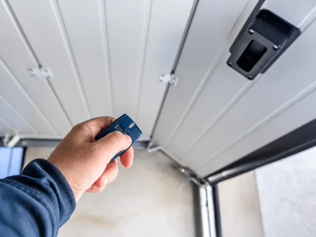 Hand holding blue garage door remote under garage door opener