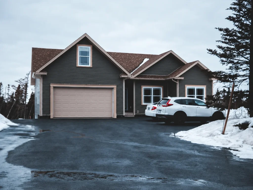 House with closed garage door, snowy driveway, and parked cars