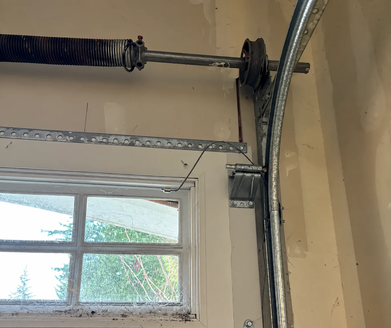 Garage door torsion spring and track beside a window, with Dan’s Garage Door Repair & Services logo overlay